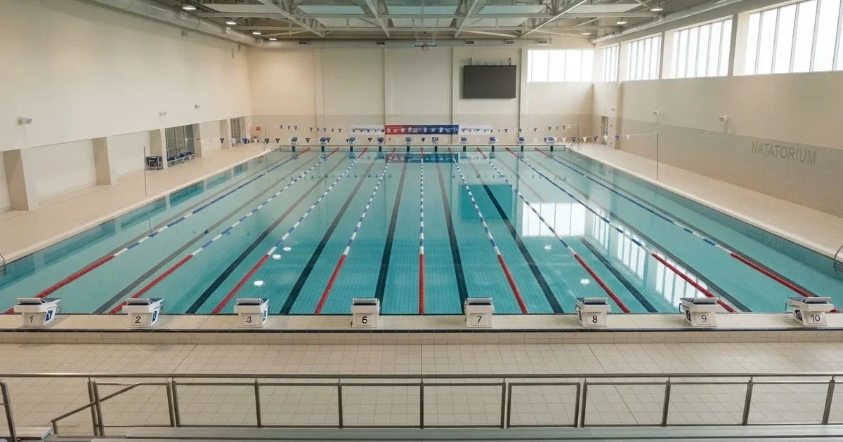 Pusty basen olimpijski z równymi torami i spokojną taflą wody, widok z trybun w jasnym świetle.
